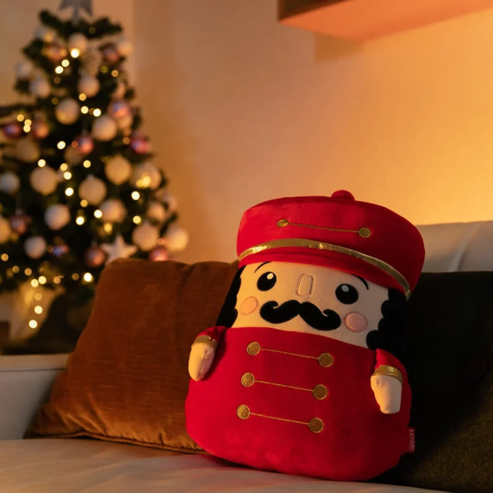 Cuscino Legami Nutcracker Super Soft rosso sul divano, con albero di Natale illuminato sullo sfondo
